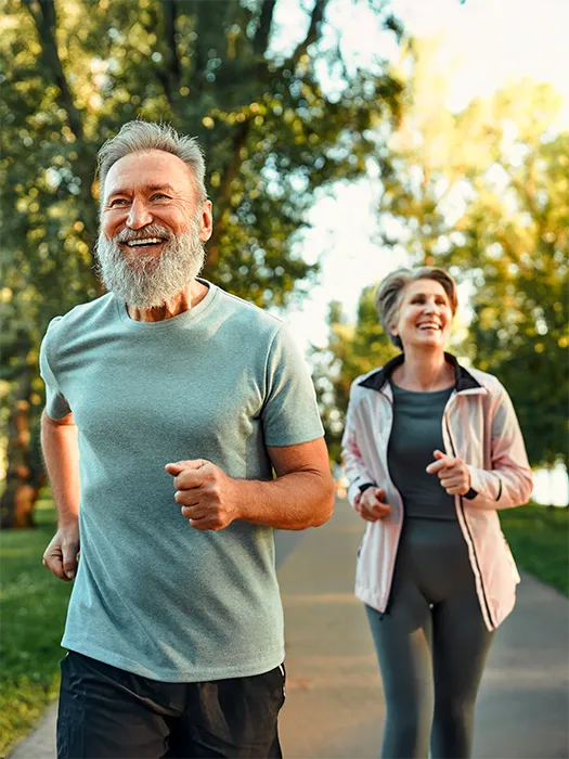 A senior couple jogging together on a tree-lined path