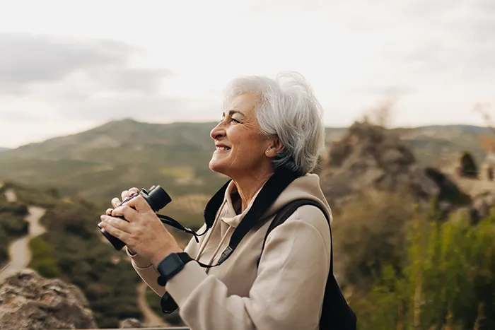 An active older woman hiking outdoors with binoculars