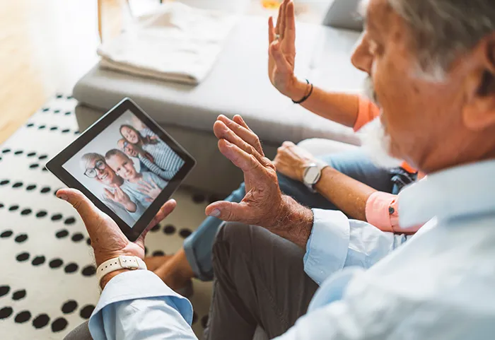 Looking over the shoulders of an older couple waving to family on a tablet video call