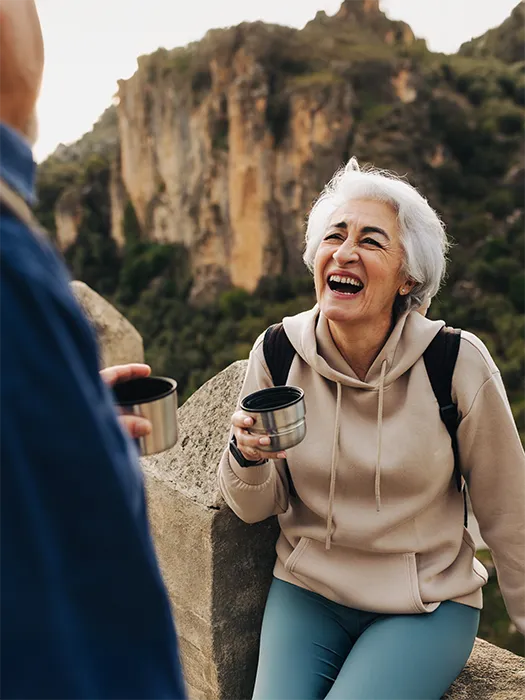 A happy older woman enjoying a hike with a companion, arms raised