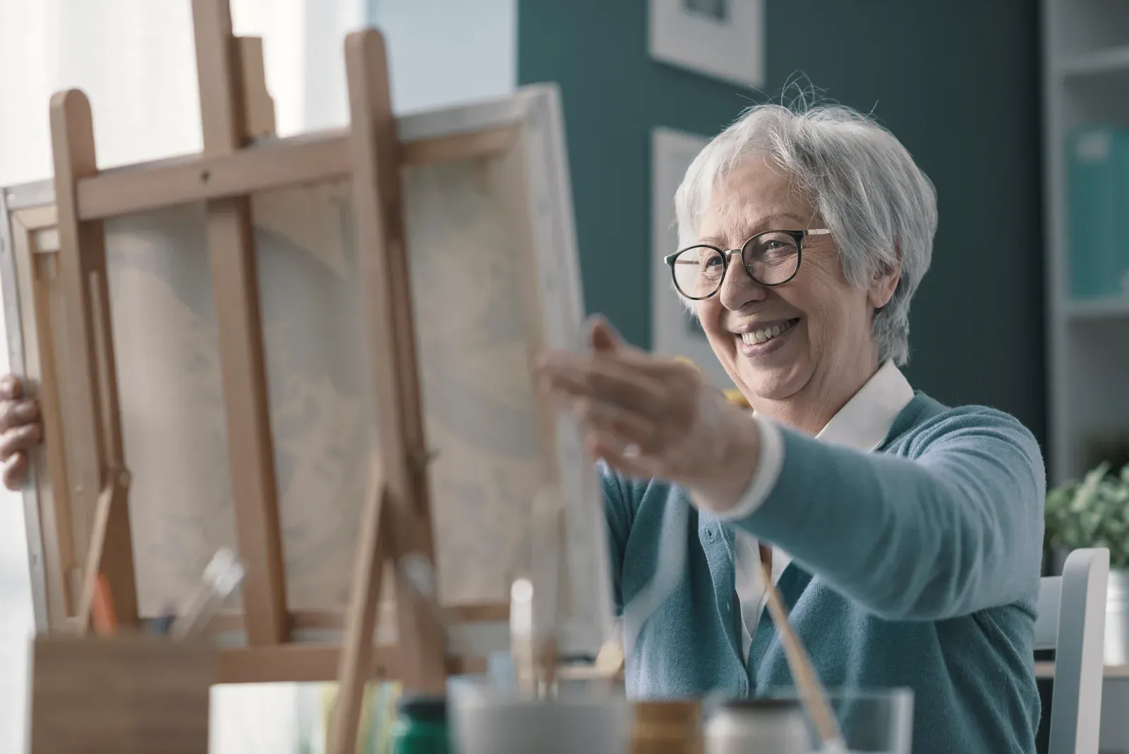 A smiling older woman placing a canvas on an easel while painting at home