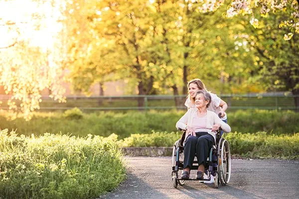 A Goldy Enrichment Specialist taking an older woman on a walk outdoors in a wheelchair