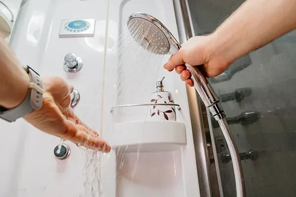 A hand testing the water temperature of a running shower
