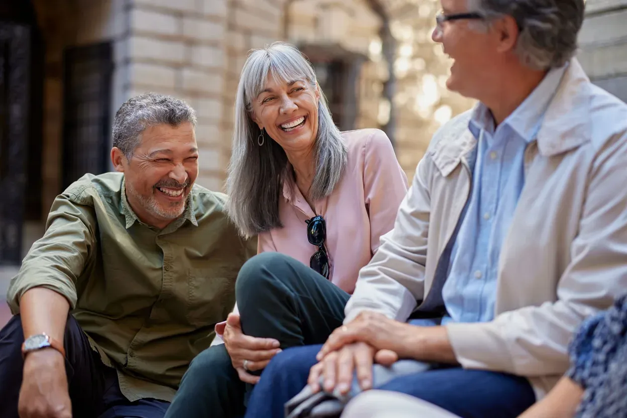 Three older friends sitting outside on a city street, laughing together